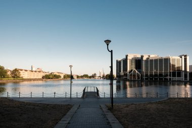 Gündoğumunda değirmen duvarının iç rıhtımının sakin sularını yansıtan modern ofis binaları. Sokak lambaları, asfalt bir yol ve Londra rıhtımlarında yer alan korkuluklar.