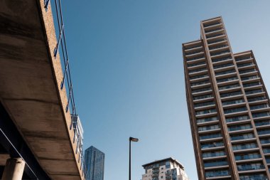 Yüksek konut binaları ve açık mavi gökyüzüne karşı yan yana uzanan beton yükseltilmiş yolun alçak açısı modern bir şehrin altyapı ve kentsel gelişiminin etkileşimini gösteriyor.