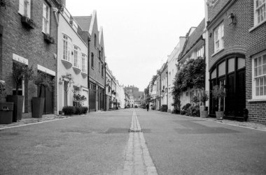 Londra 'daki Kynance Mews' in sakin atmosferini yansıtan tek renkli kareli film fotoğrafı. Uzakta zarif evler ve yalnız bir yaya var.