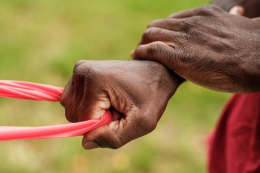 Tarımsal uygulamalarda kullanılması muhtemel bir parça kırmızı plastiği kavrayan ve geren bir çiftçinin ellerinin yakın plan görüntüsü, bulanık yeşil bir arka plan, bir çiftlik ya da tarla düzeneği öneriyor.