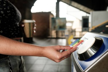 Metro biletini kredi kartıyla ödeyen bir turist, elinde tek kullanımlık bir kahve fincanı olan, ulaşılamayan ödemelerle metro istasyonuna giren bir turist.