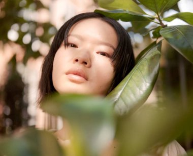 Botanik bahçesinde tropik yaprakların arkasında poz veren güzel Asyalı genç bir kadının orta formatlı film portresi. Güneş ışığı ve temiz havanın tadını çıkarıyor.