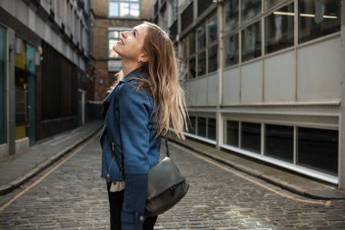 Londra 'da büyüleyici bir kaldırım taşından sokakta yürüyen genç ve mutlu bir kadın. Etrafını saran güzel binalara bakarken gülümsüyor.