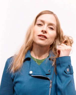 Mavi ceket giyen, beyaz arka planda saçlarıyla oynayan, analog tahıl ve klasik titreşimler içeren sarışın bir kadının orta formatlı film portresi.