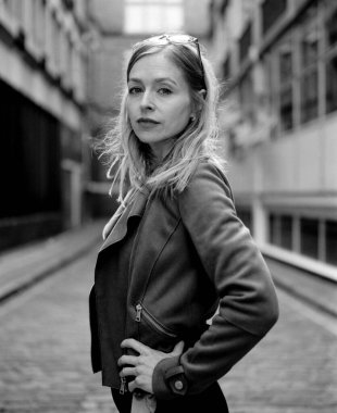 Kafasında güneş gözlüğü olan şık bir kadın dar bir şehir geçidinde güven içinde poz veriyor, çarpıcı bir monokrom formatında, analog bir fotoğrafta görülüyor.