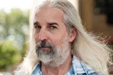 Uzun gri saçlı, sakallı, bilgelik ve deneyim saçan kendinden emin yaşlı bir adamın yakın plan portresi.