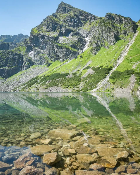 Prominent rocky mountain reflecting in crystal clear alpine lake, vertical shot, Poland, EU.