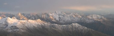 Turuncu günbatımında yüksek zirveleri olan karlı sıradağların panoramik görüntüsü, Avusturya Alpleri, Avrupa.