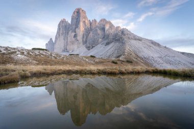 Tre Cime 'nin devasa kaya oluşumunun üzerinde batan güneş, İtalya' nın Dolomitler adasında küçük bir gölete yansıyor..