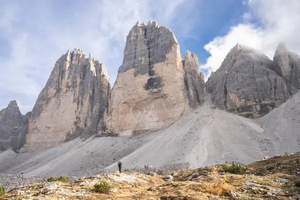 Photographer standing below massive rock towers formation of Tre Cime, Dolomites, Italy.