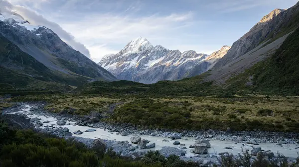 Buzul nehrinin aktığı manzaralı Alp Vadisi. Gün batımında arka planda belirgin bir tepe noktası..