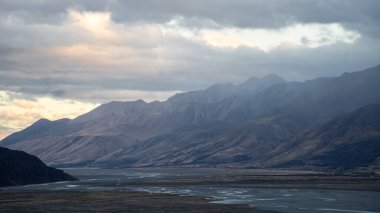 Alp Vadisi 'ndeki dağ sıraları renkli günbatımı ve üzerinde fırtına bulutları olan Yeni Zelanda..