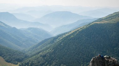 Slovakya, Avrupa 'da çekilen, arka planda dağ katmanları olan büyük bir kayanın üzerinde dinlenen yürüyüşçü..