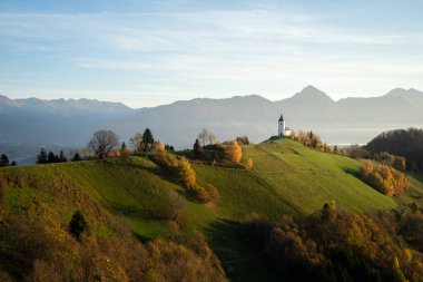 Tepede küçük bir kilise ve arka planda dağlarla dolu resim gibi dağlık bir manzara, Slovenya.