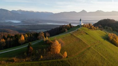 Tepede küçük bir kilise ve arka planda dağlarla dolu resim gibi dağlık bir manzara, Slovenya.