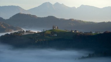 Slovenya dağının tepesinde orman, sis ve küçük kiliseyle güzel bir sabah manzarası, Avrupa.