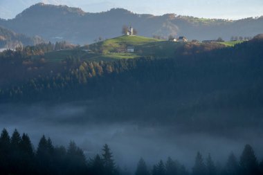 Slovenya dağının tepesinde orman, sis ve küçük kiliseyle güzel sonbahar manzarası, Avrupa.