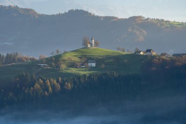 Slovenya dağının tepesinde orman, sis ve küçük kiliseyle güzel sonbahar manzarası, Avrupa.