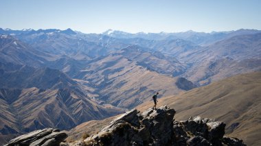 Arkaplanda dağ katmanları olan kayalık tepelerde yürüyen yürüyüşçü, Yeni Zelanda.