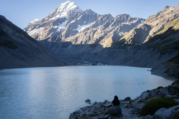 Buzul gölü kıyısında oturan bir kadın buzullara ve dağlara bakıyor. Cook Dağı, Yeni Zelanda..