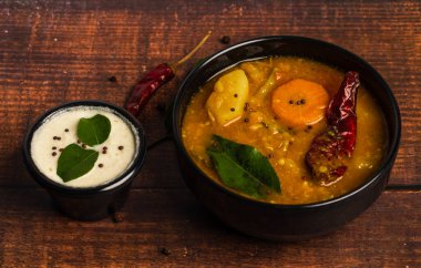 Sambar şat ve hindistan cevizi turşusu ahşap arka planda siyah kaseler üzerine dizilmiş. Sambar ve turşu Güney Hindistan ve Sri Lanka mutfağında popülerdir..