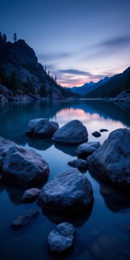 Büyük kaya ve kayaların olduğu sakin bir manzara alacakaranlıkta kısmen sakin ve yansıtıcı bir göle battı. Gökyüzü masmavi.