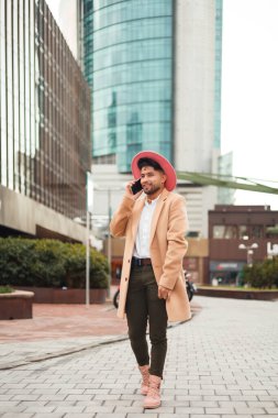 Genç stil sahibi adam yürüyor ve akıllı telefon kullanıyor, dikey çekim