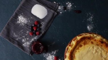 Hands placing cheesecake on table with strawberry jam, blueberries and raspberries, overhead view. Slow motion fhd footage.