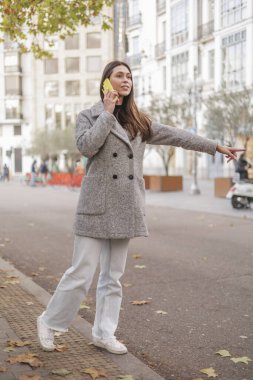 Genç Latin kadın otobüsü arıyor ve akıllı telefon kullanıyor. Yaşam tarzı gibi görünüyor. Yüksek kalite fotoğraf