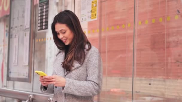 黄色いスマートフォンを使用してバス停で待っている美しいブラジル人女性 高品質の写真 — ストック動画