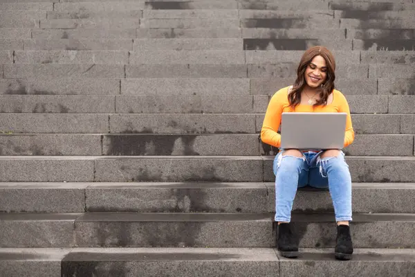 Üniversite merdivenlerinde dizüstü bilgisayar kullanan transseksüel kadın öğrenci. Merdiven boşluğunu kopyala. Yüksek kalite fotoğraf