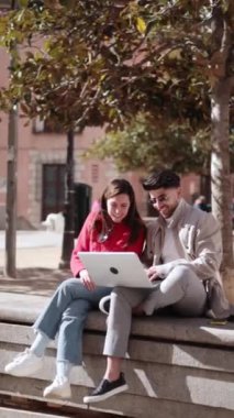 Güneşli bir günde parkta dizüstü bilgisayar kullanan iki öğrenci arkadaş. Çalışıyorlar ve gülümsüyorlar. Yüksek kaliteli FullHD görüntüler