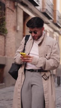 Şehir caddesinde yürüyen ve akıllı telefon kullanan şık bir Kolombiyalı. Yüksek kaliteli FullHD görüntüler
