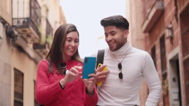 Sokakta cep telefonu kullanan neşeli, genç bir Latin çift. Yüksek kaliteli FullHD görüntüler