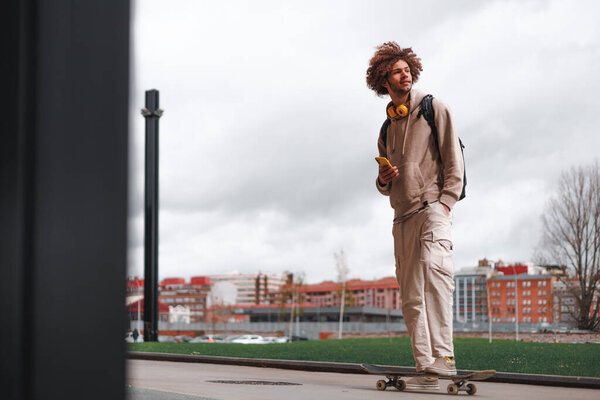 Молодой кудрявый европеец с мобильным телефоном, смотрящим в небо. Небо фон. Вертикальное копировальное пространство. Высокое качество фото