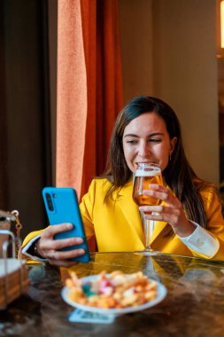 Modern barda bira içerken cep telefonu kullanan moda bir kadın. Metin için dikey boşluk. Yüksek kalite fotoğraf