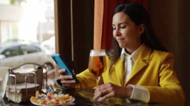 Modern barda bira içerken cep telefonu kullanan modaya uyan beyaz bir kadın. Yüksek kalite fotoğraf