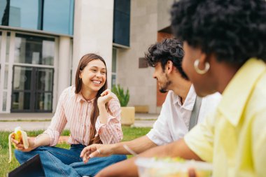 Latin üniversite öğrencileri kampüste oturmuş sohbet ediyor ve gülümsüyor. Yüksek kalite fotoğraf