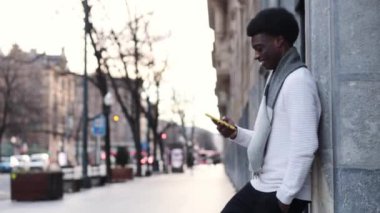 Duvara yaslanan ve cep telefonu kullanan yakışıklı Afrikalı bir adamın yan görüntüsü. Yüksek kalite fotoğraf