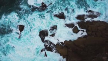 Havadan çekilen güzel turkuaz dalgaların kayalık kayalıklara çarpması. Yüksek kalite 4k görüntü