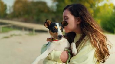 Genç bir kadın köpeğine sarılıyor ve nehire yakın bir yolda durup gülüyor.