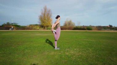 Serene Park ortamında bacak esnetme egzersizleri yapan genç bir kadın.