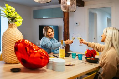 Evde romantik bir sevgililer günü yemeğinde beyaz şarapla kadeh kaldıran iki kadın.