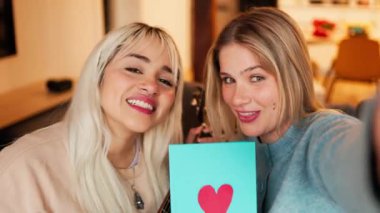 Mutlu lezbiyen çift gitar çalarken selfie çekiyor ve ellerinde sevgililer günü kartı tutuyor.