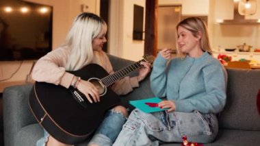 İki kadın kanepede oturup gitar çalıyor ve sevgililer günü hediyelerini değiş tokuş ediyorlar.