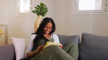 Evdeki kanepesinde dinlenirken tablet kullanan rahat bir genç kadın.