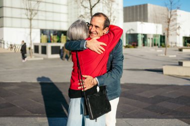 Üst düzey arkadaşlar güneşli bir açık hava toplantısında neşeyle kucaklaşıyorlar.