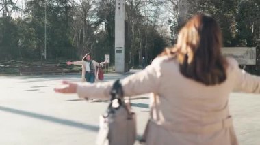 İki bayan arkadaş alışveriş yaparken el sallıyor ve parkta buluşuyorlar.