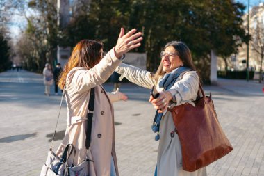 Şehir merkezinde alışveriş yaptıktan sonra kucaklaşan iki olgun kadın.