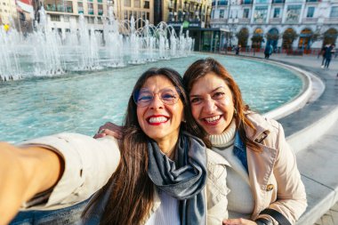 İki mutlu olgun kadın Valladolid, İspanya 'da bir çeşmenin yanında selfie çekiyor ve tatillerinin tadını çıkarıyorlar.